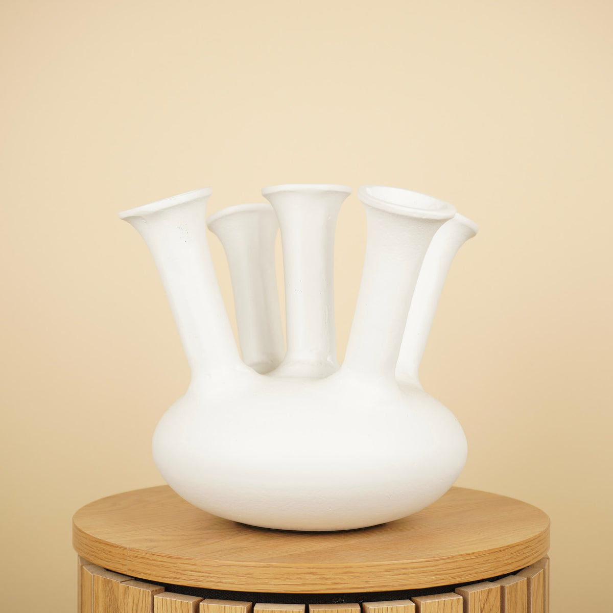 Witte tulpenvaas met ronde buik en vijf lange, uitlopende halzen op een ronde houten tafel.
