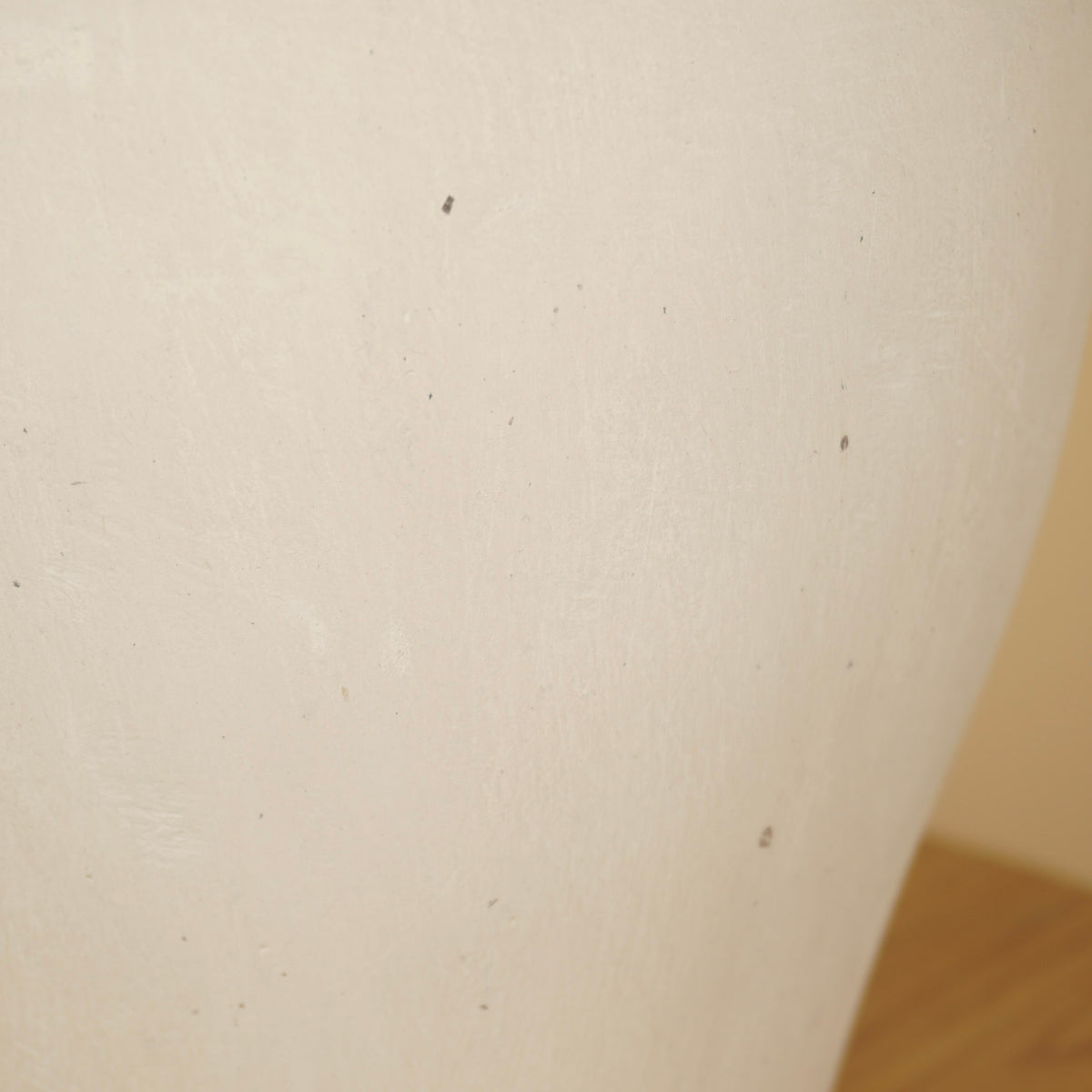 Detail van het matte oppervlak van een crèmekleurige vaas met fijne structuur en kleine donkere spikkels.