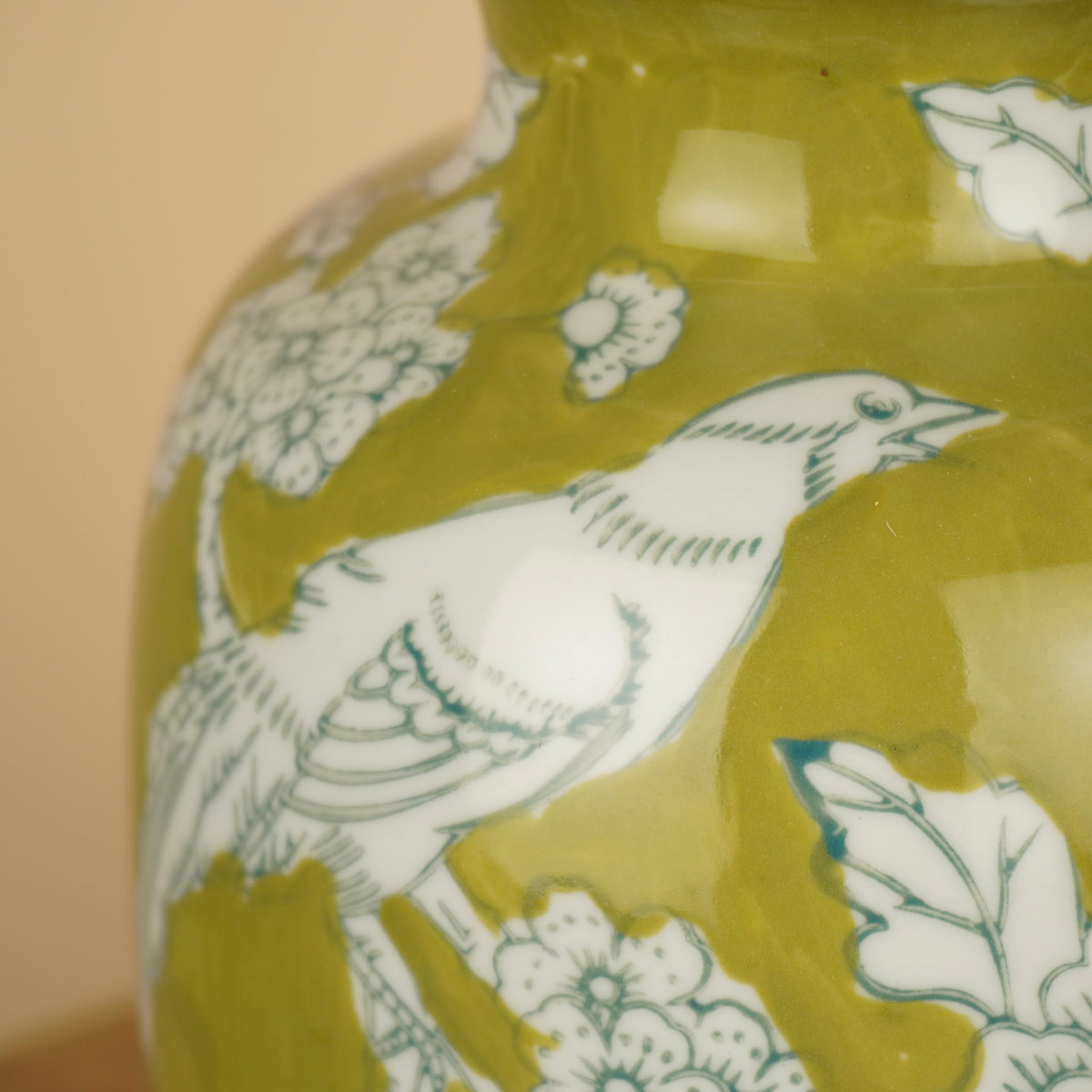 Detail van een witte vogel, bloemen en bladeren op een glanzende groene vaas.