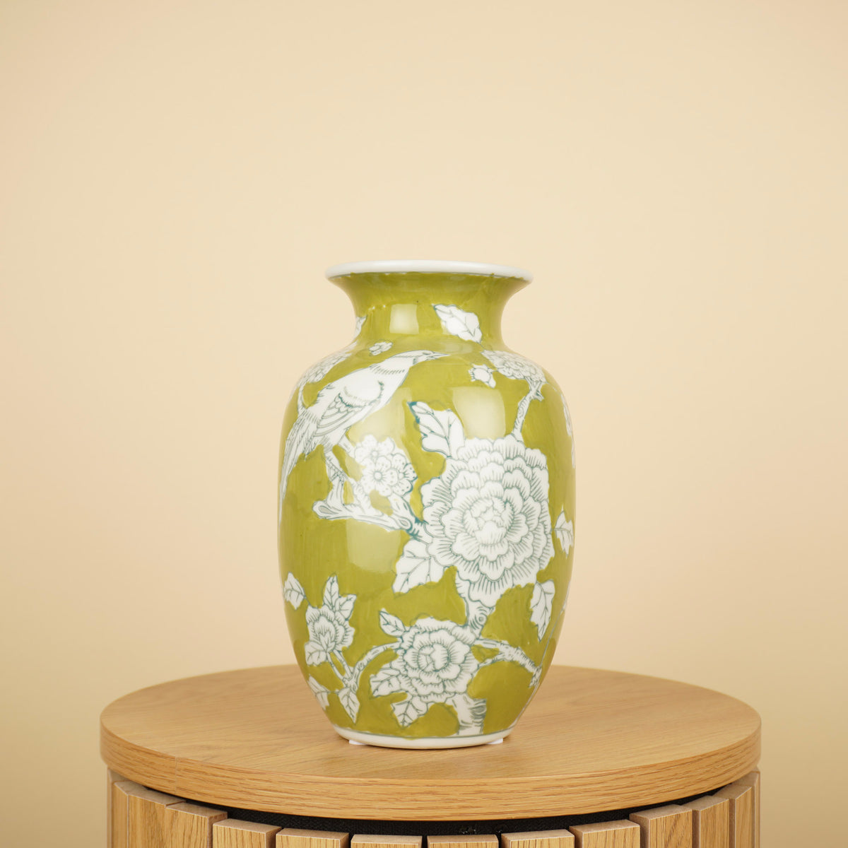 Groene vaas met witte bloemen en vogelmotief op een ronde houten tafel.