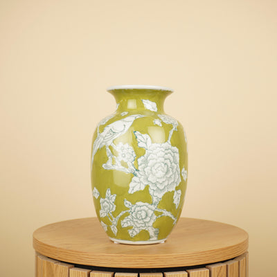 Groene vaas met witte bloemen en vogelmotief op een ronde houten tafel.