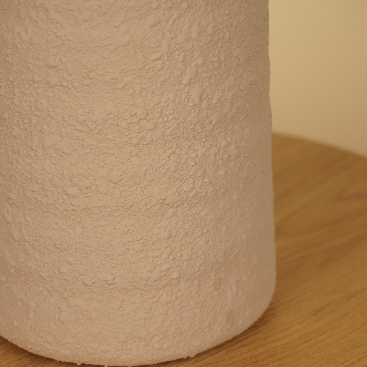 Detail van het ruwe, korrelige oppervlak en de afgeronde onderrand van een beige vaas.