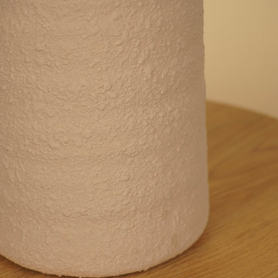 Detail van het ruwe, korrelige oppervlak en de afgeronde onderrand van een beige vaas.