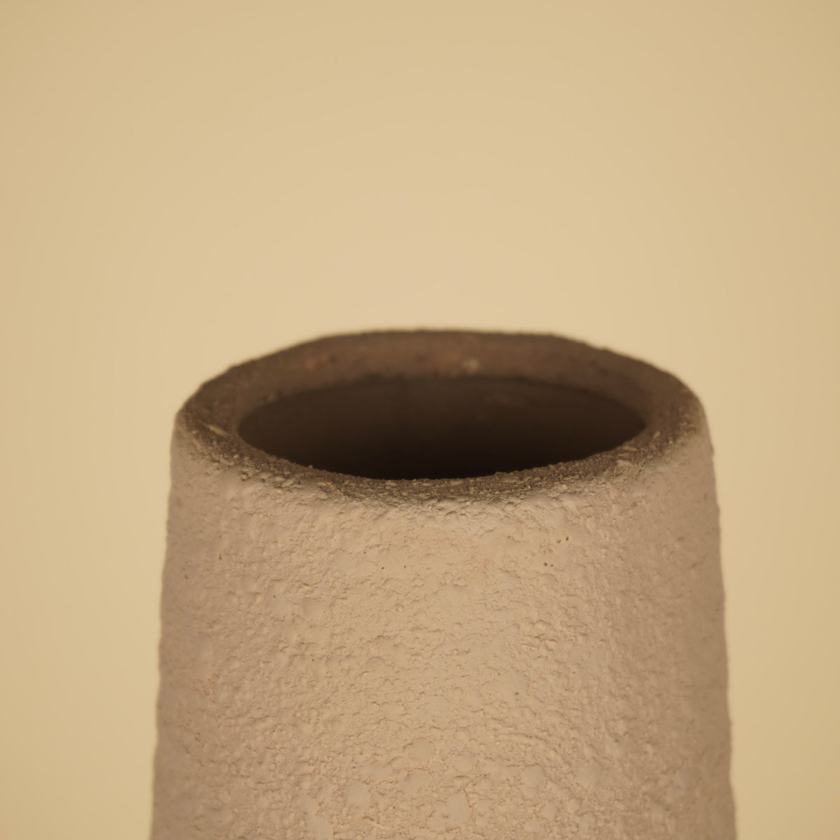 Detail van de smalle ronde opening met dikke, ruwe rand en donkere binnenzijde van een beige vaas.