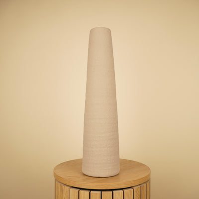Hoge, slanke beige vaas met taps toelopende vorm en ruwe structuur op een ronde houten tafel.