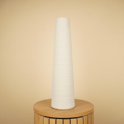 Hoge, slanke witte vaas met taps toelopende vorm en ruwe structuur op een ronde houten tafel.