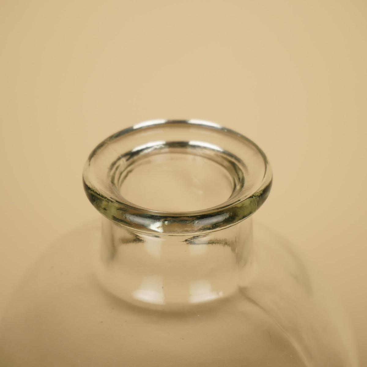 Detail van de smalle ronde opening met dikke, afgeronde glazen rand van een transparante flesvaas.