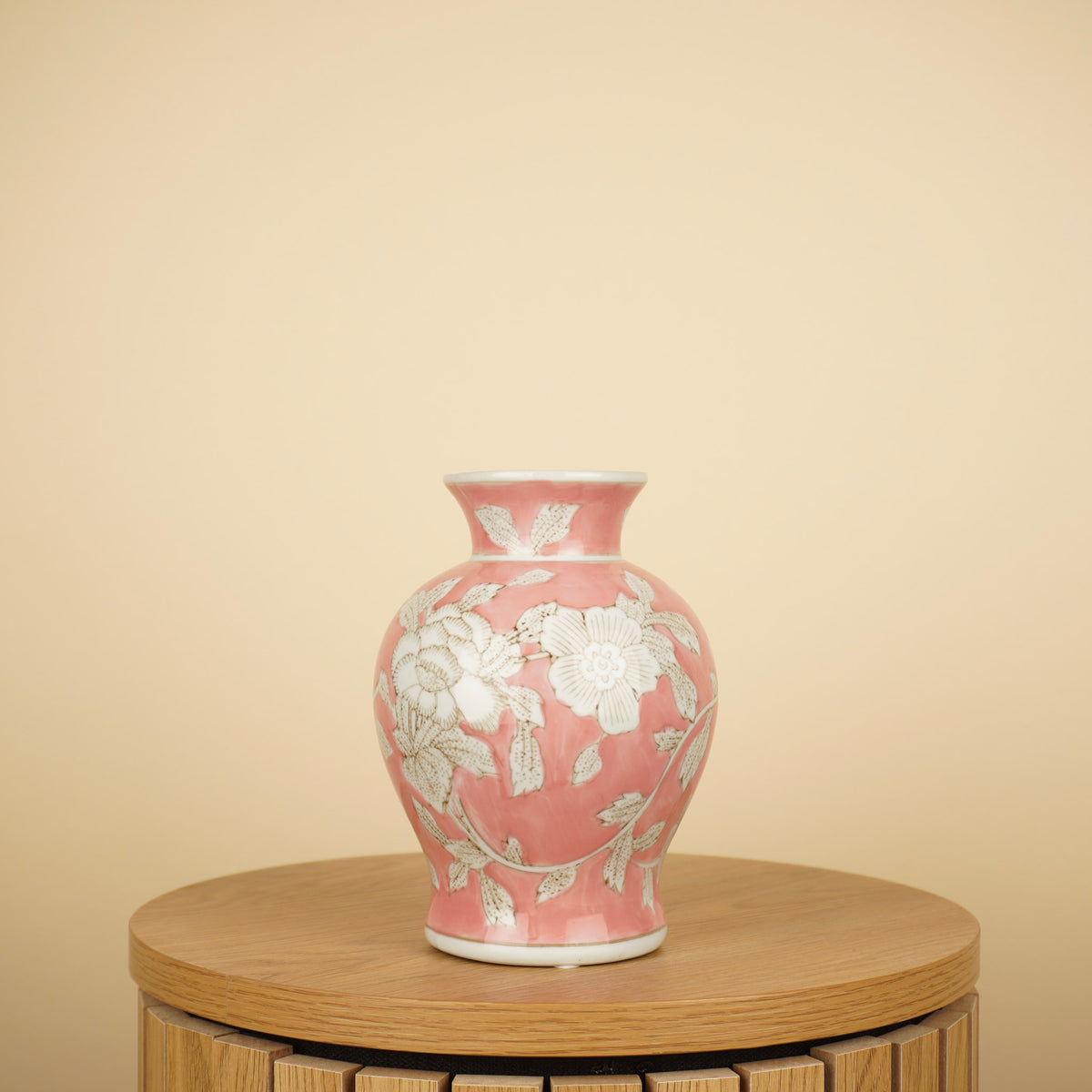 Roze vaas met witte bloemen en bladeren, een smalle hals en uitlopende rand op een ronde houten tafel.