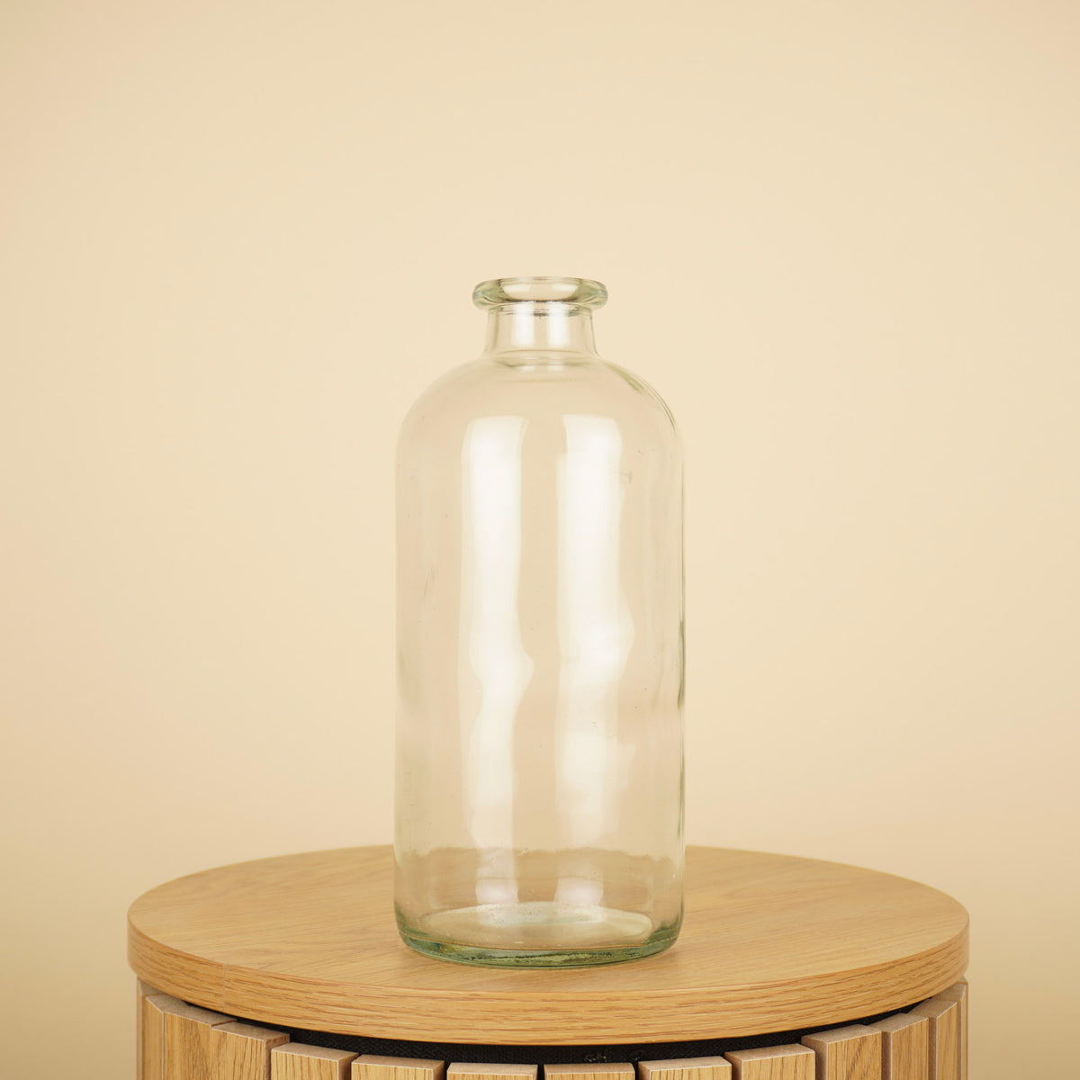 Transparante glazen flesvaas met ronde schouders en een korte, smalle hals op een houten tafel.