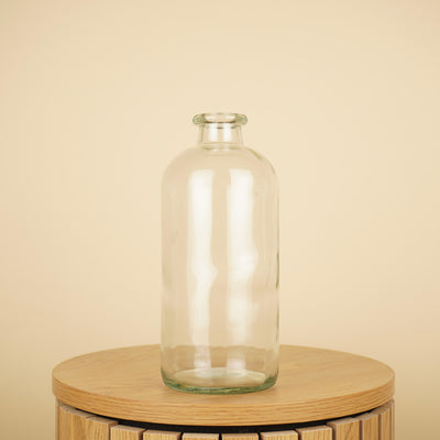 Transparante glazen flesvaas met ronde schouders en een korte, smalle hals op een houten tafel.