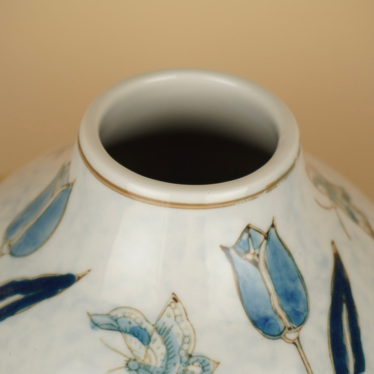 Detail van de ronde opening met goudkleurige lijn op een witte vaas met blauwe tulpen en vlinders.
