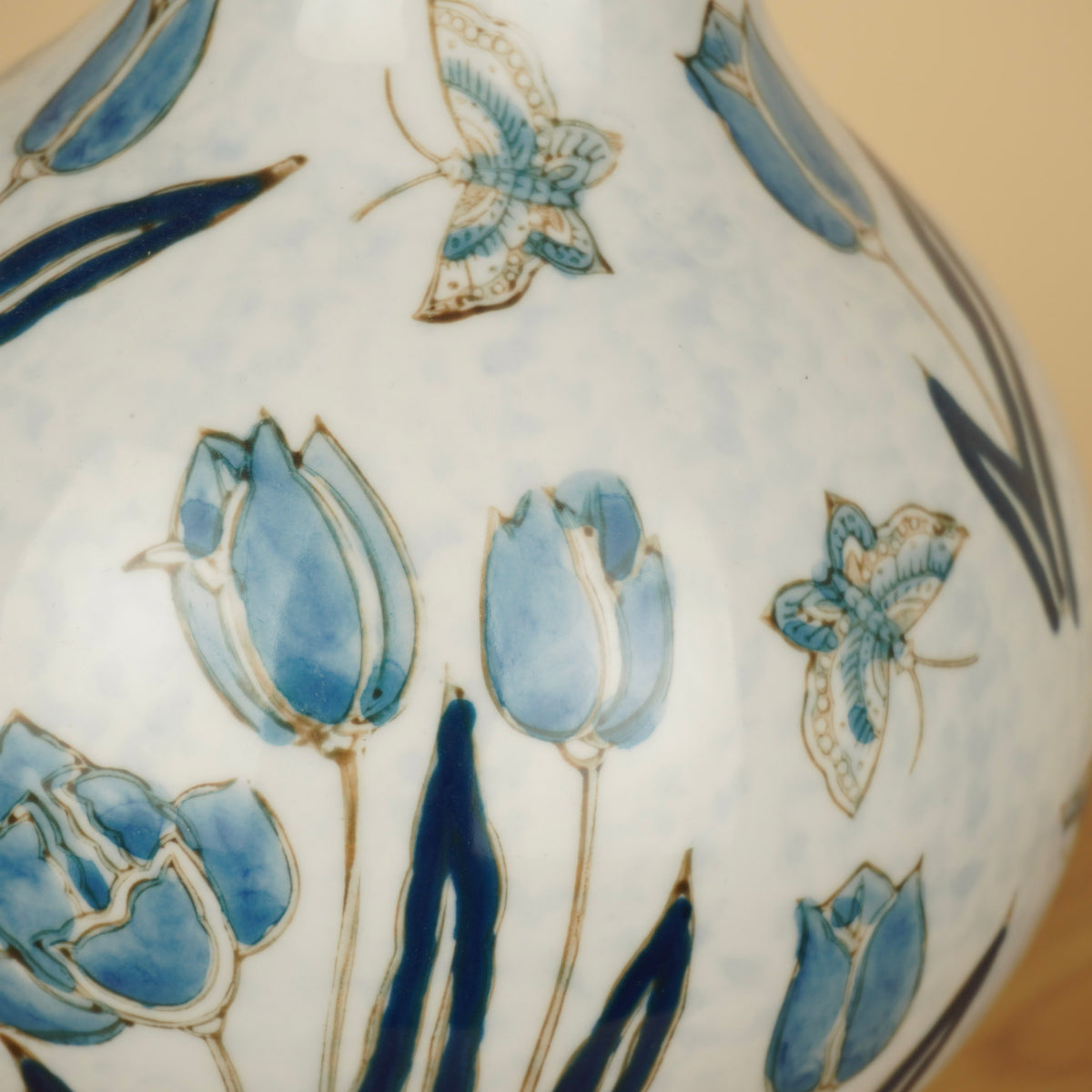 Detail van blauwe tulpen, donkerblauwe bladeren en vlinders op de glanzende witte vaas.